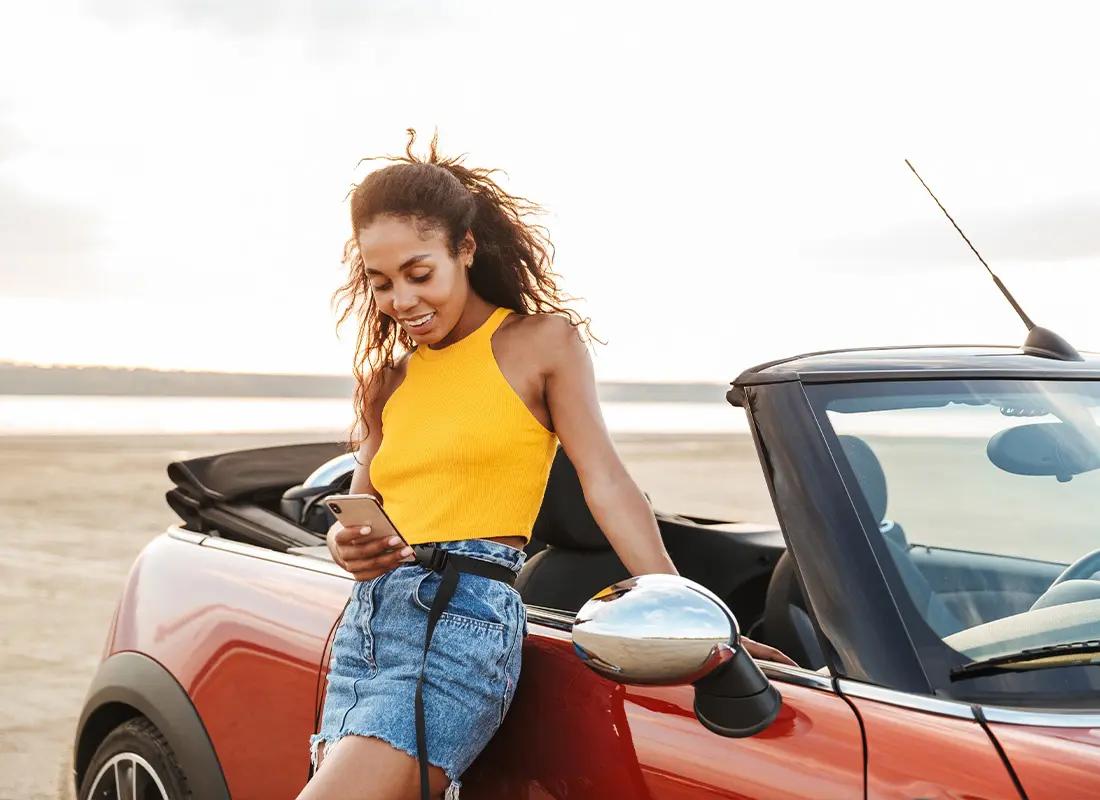 About-Our-Agency-A-Young-Woman-Smiling-at-Her-Phone-While-Resting-Beside-Her-Car