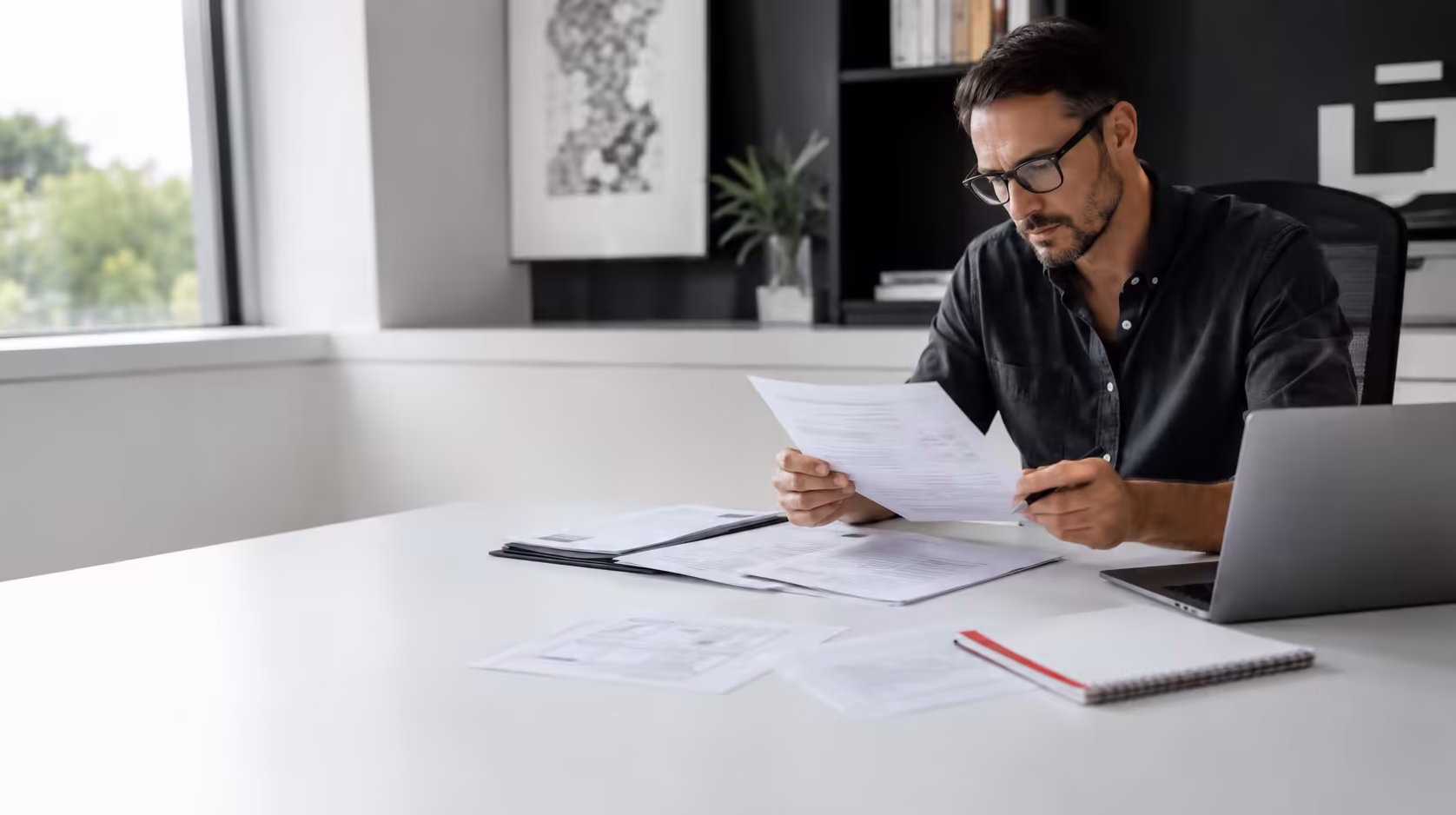 Professional-services business owner reviewing client work and insurance documents at a desk.